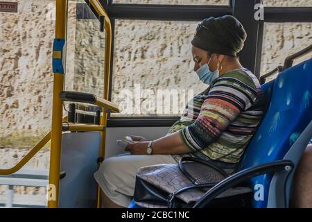 Jerusalem, Israel - 6. August 2020: Eine jüdische orthodoxe Frau, die eine COVID-Maske trägt und ihre Busfahrt zum Gebet nutzt. Stockfoto