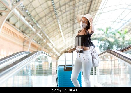 Tourist Frau mit Gepäck und Reisezubehör auf der Rolltreppe eines Transportstation. Sie trägt eine Gesichtsmaske als vorbeugende Maßnahme. Platz für te Stockfoto