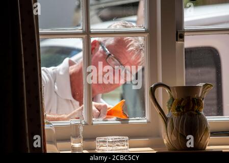 Hampshire, England, Großbritannien. 2020. Maler mit einem Schaber, um die Fenster für die Malerei von innerhalb des Grundstücks gesehen vorzubereiten. Stockfoto