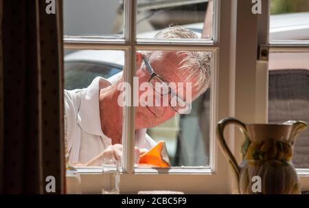 Hampshire, England, Großbritannien. 2020. Maler mit einem Schaber, um die Fenster für die Malerei von innerhalb des Grundstücks gesehen vorzubereiten. Stockfoto