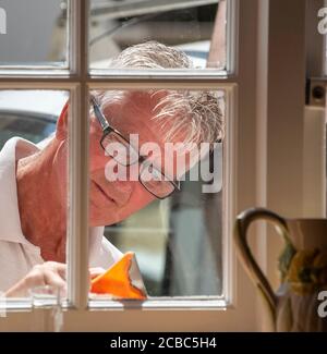 Hampshire, England, Großbritannien. 2020. Maler mit einem Schaber, um die Fenster für die Malerei von innerhalb des Grundstücks gesehen vorzubereiten. Stockfoto