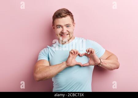 Glücklich stark muskulösen Mann trägt casual blau T-Shirt über isoliert rosa Hintergrund lächelnd in der Liebe zeigt Herz Symbol und Form mit Händen. Romanti Stockfoto