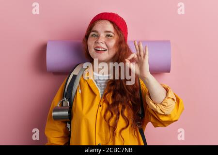 Junge glücklich positive Frau trägt Rucksack tun ok Zeichen mit Fingern, ausgezeichnetes Symbol über isolierten rosa Hintergrund. Körpersprache. Nahaufnahme Stockfoto