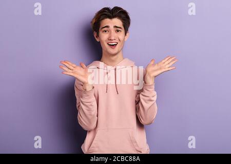Portrait von zwei jungen überrascht emotionale ahnungslos verwirrt Mann in rosa stilvolle Sweatshirt hält Palmen in der Nähe Wangen, über blauem Hintergrund stehen. cl Stockfoto