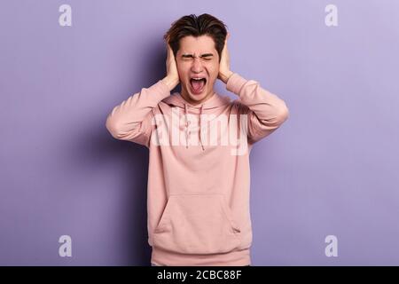 Junger verrückter lustiger emotionaler Mann, der seine Ohren bedeckt und schreit.junger Mann, der schreit, will nicht auf seine Frau hören Stockfoto
