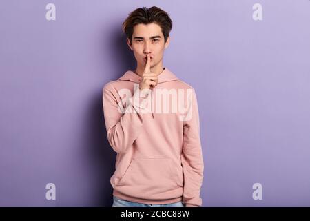 Junger schöner Mann trägt rosa stilvolle Sweatshirt über isolierten blauen Hintergrund bitten, ruhig mit Finger auf den Lippen zu sein. Stille und geheimes Konzept.bo Stockfoto