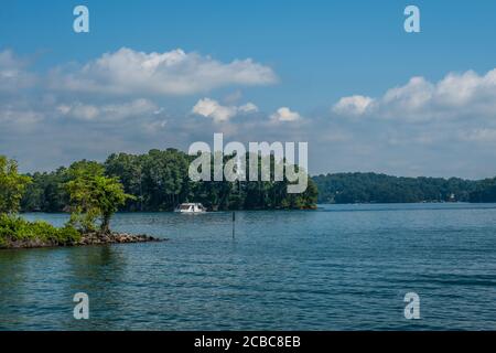 Ein Hausboot, das an einer der Inseln vorbei fährt see mit anderen Motorbooten im Hintergrund auf einem hellen Heißer Tag im Sommer Stockfoto