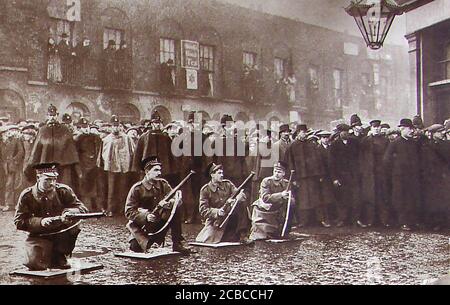 Seige of Sidney Street - die Belagerung der Sidney Street (Januar 1911), auch bekannt als die Schlacht von Stepney, nahm am East End von London zwischen der britischen Polizei von Soldaten unterstützt, nach einem Raub und der Ermordung von drei Polizisten durch lettische revolutionäre. Dieses historische Foto zeigt Soldaten, die ihre Gewehre mit Massen von Zuschauern beladen, die von britischen Polizisten ("Bobbies") zurückgehalten werden. Stockfoto