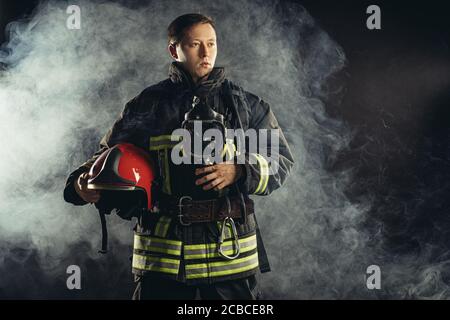 Tapferer Feuerlöscher oder Feuerwehrmann in dunkler Schutzkleidung Uniform, mit Helm auf dem Kopf, mit Seilen, Hammer und andere spezielle Ausrüstung bei der Arbeit Stockfoto