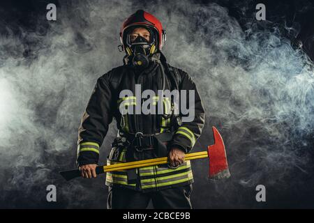 Junge Feuerwehrmann Vorbereitung zu retten, Feuer zu löschen und Menschen zu retten, wenn nötig, mit Hammer in den Händen und tragen Schutzanzug Uniform Stockfoto