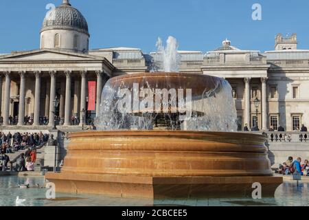 Nahaufnahme eines der beiden Springbrunnen des Trafalgar Square London mit dem National Gallery Museum im Hintergrund vor einem blauen Winterhimmel. Stockfoto