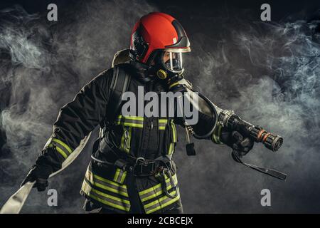 Tapferer Feuerlöscher oder Feuerwehrmann in dunkler Schutzkleidung Uniform, mit Helm auf dem Kopf, mit Seilen, Hammer und andere spezielle Ausrüstung bei der Arbeit Stockfoto