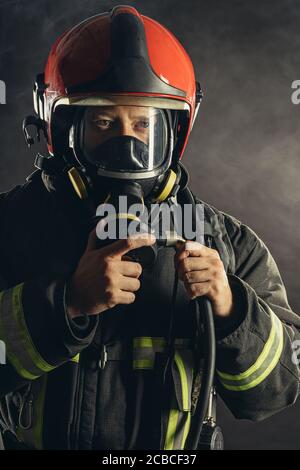 Portrait von selbstbewussten tapferen Feuerlöscher in Schutzuniform tragen roten Helm und Blick auf Kamera posiert, schwarzer Hintergrund Stockfoto