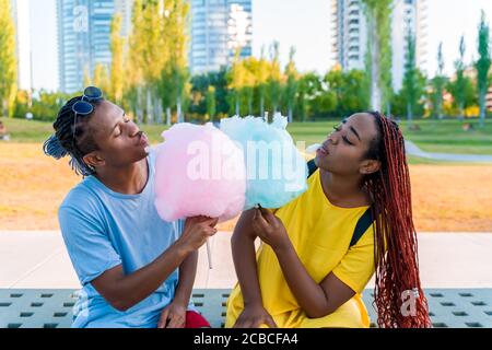 Ein glückliches schwarzes Paar, das bunte Zuckerwatte zusammen in einem Park einer großen Stadt hat. Stockfoto