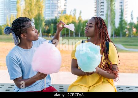 Ein glückliches schwarzes Paar, das bunte Zuckerwatte zusammen in einem Park einer großen Stadt hat. Stockfoto