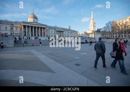 Touristen gesehen zu Fuß auf dem weiten Raum des Trafalgar Square mit der National Gallery Museum und Kirche St. Martin in den Feldern im Hintergrund. Stockfoto