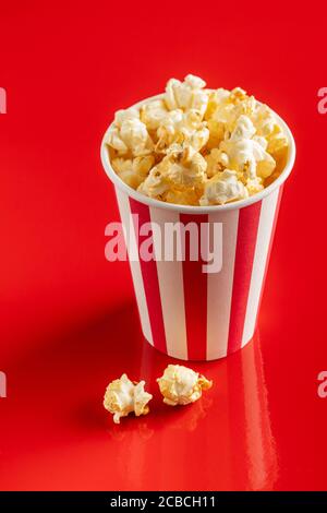 Süßes Popcorn im gestreiften Pappbecher auf rotem Hintergrund. Stockfoto