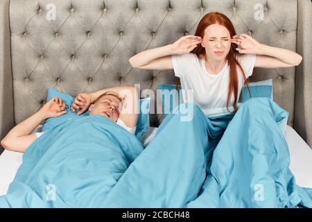 Wütend Ingwer Frau mit geschlossenen Augen auf dem Bett sitzen. Mädchen will nicht zu ihrem Mann Schnarchen hören. Nahaufnahme Foto Stockfoto