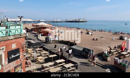 Brighton, Großbritannien - 10. August 2020: Karussells und Unterhaltung auf dem Abschlussball und Menschen am Strand genießen das heiße Wetter. Stockfoto