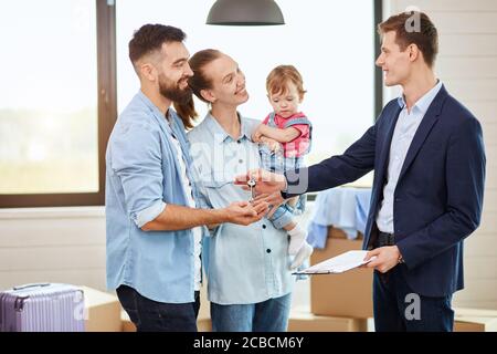 Kaukasische Familie von drei Personen nehmen Schlüssel neues großes Haus von realtor. Sie lächeln. Hintergrund bewegliche Kästen, großes Fenster. Stockfoto