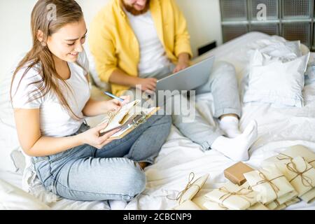 Glücklich kaukasischen Ehepaar Sortierung Briefe zu Hause, sie gehen, um Gäste in ihr neues Haus einladen, housewarming. Sie machen Notizen auf Laptop und PR Stockfoto