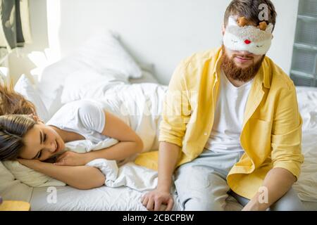 Schläfriger Mann sitzen neben schlafende Frau, muss morgens zur Arbeit gehen. Sitzen Sie in Maske zum Schlafen neben Frau Stockfoto