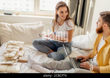 Glücklich kaukasischen Ehepaar Sortierung Briefe zu Hause, sie gehen, um Gäste in ihr neues Haus einladen, housewarming. Sie machen Notizen auf Laptop und PR Stockfoto