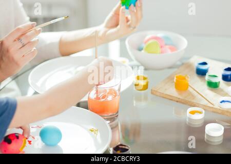 Hausgemachte Ostern Dekorationen und kleinen Helfer. Selektiver Fokus der kleinen Hände eines Jungen, gekochte Eier mit bunten Farben auf weißem Schild Stockfoto