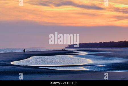 Ein paar Leute genießen einen ruhigen Strandspaziergang auf Hilton Island während eines gedeckten, winterlichen Sonnenuntergangs Stockfoto