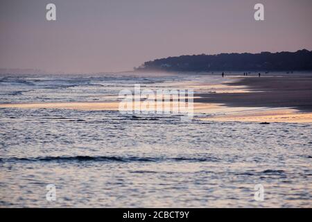 Gedämpfte Farben des Winteruntergangs an einem Strand auf Hilton Head Island spiegeln sich in Wellen wider, die sich in die Deckung stürzen Der Sand Stockfoto