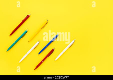 Sieben bunte Kugelschreiber auf hellgelbem Hintergrund. Draufsicht, Kopierbereich für Text. Zurück zur Schule Konzept Stockfoto