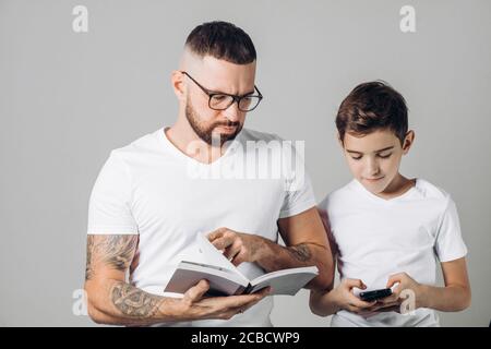 Junge gut aussehende kluge Papa hilft seinem Sohn mit Hausaufgaben, während der Junge im Netz surft, Kind die Antworten, Schlüssel des Schulbuchs, durchsucht. Stockfoto