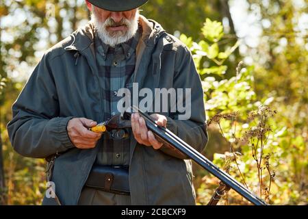 Senior Jäger laden Gewehr und gehen zu schießen. Mann in Jagd Freizeitkleidung, Herbst Wald Hintergrund Stockfoto