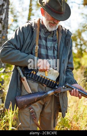 Fowler hält Schrotflinte, Patronen auf dem unteren Rücken, bereit, auf Vögel zu schießen. Waldhintergrund Stockfoto