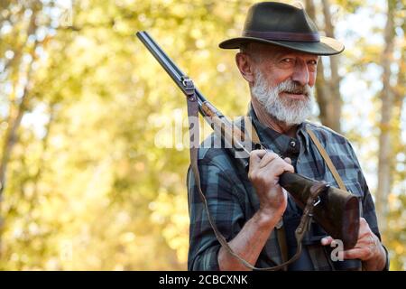 Happy Senior Hunter Lächeln nach immer gut, große Trophäe im Wald. Jagd auf wilde Tiere, Vögel. Zufriedener Jäger mit grauem Bart, mit Schrotflinte Stockfoto