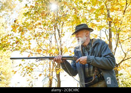 Konzentrierter Jäger hält Gewehr und wartet auf Beute, Jäger schießen im Herbstwald. Jagdsaison Stockfoto