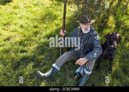 Auf der Suche nach Trophäe mit Hund. Älterer Mann bereit zur Jagd. Sitzen und ruhen vor der Jagd Stockfoto