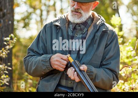 Senior Jäger laden Gewehr und gehen zu schießen. Mann in Jagd Freizeitkleidung, Herbst Wald Hintergrund Stockfoto