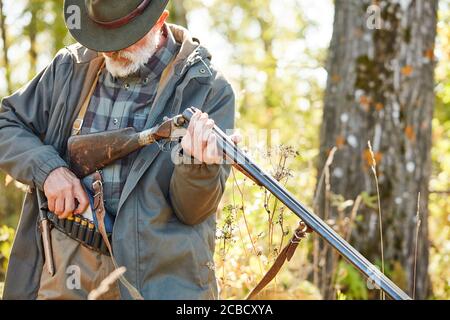 Senior Jäger laden Gewehr und gehen zu schießen. Mann in Jagd Freizeitkleidung, Herbst Wald Hintergrund Stockfoto