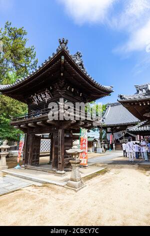 Glockenturm und Tor bei Enmyoji - Tempel Nr. 53 auf der Shikoku Pilgerfahrt. Der Tempel hat Fliesenskulpturen auf den Dächern seiner Gebäude mit Wheel of DH Stockfoto