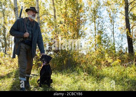 Älterer Mann auf der Jagd mit seinem Hund im Wald, sonniges Wetter, auf der Suche nach Trophäe Stockfoto