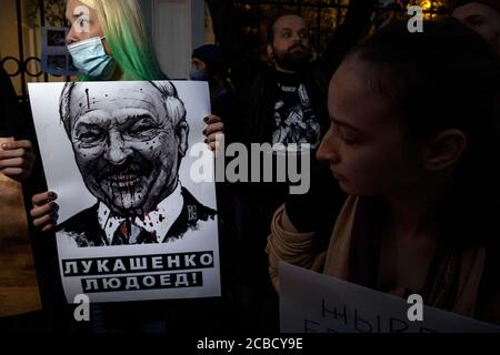 Moskau, Russland. 12. August 2020 EINE Frau hält Plakate mit dem belarussischen Präsidenten Alexander Lukaschenko vor der belarussischen Botschaft während eines Protestes gegen die Ergebnisse der belarussischen Präsidentschaftswahl in Moskau, Russland. Auf dem Banner steht: "Lukaschenko ist ein Kannibaler" Stockfoto