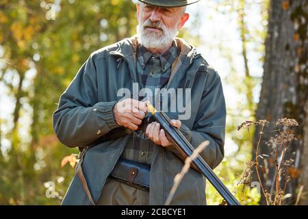 Ältere Jäger laden Gewehr und gehen zu schießen. Mann in Jagd Freizeitkleidung, Herbst Wald Hintergrund Stockfoto