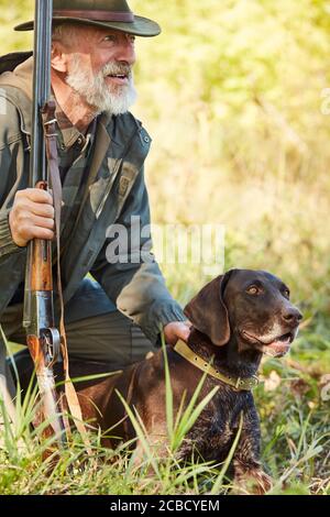 Jagdsaison. Senior Jäger Mann mit Pistole sitzen auf dem Boden mit labrador. Jagdkonzept Stockfoto