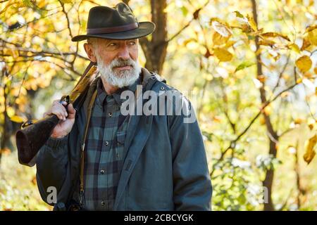 Waldjagd auf Tiere. Älterer Mann mit Schrotflinte, schaut weg. Aufgeregt nach der Jagd im Wald Stockfoto