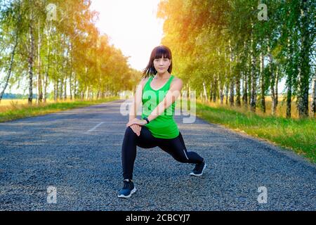 Junge Frau, die sich die Beine vor dem Joggen auf Asphaltstraße streckt Stockfoto