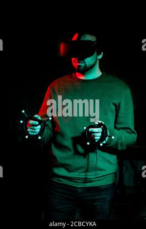 Ein junger Mann spielt mit Virtual-Reality-Ausrüstung in einem Dunkles Zimmer Stockfoto