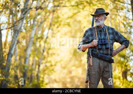 Bärtiger kaukasischer Jäger mit Cowboy-Hut auf der Suche nach Trophäe im Herbstwald. Stand auf der Suche nach Beute in der Jagdzeit, Herbstsaison geöffnet. Stockfoto