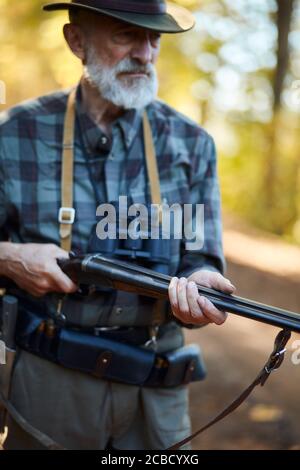 Älterer Jäger Mann mit grauem Bart halten Waffe auf Vögel jagen, bereit zu schießen. Waldhintergrund Stockfoto