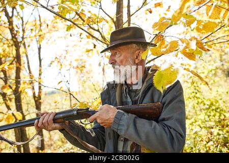 Konzentrierter Jäger hält Gewehr und wartet auf Beute, Jäger schießen im Herbstwald. Jagdsaison Stockfoto